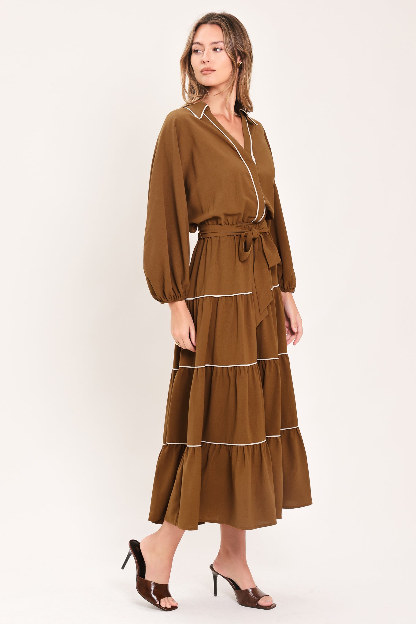 A woman wearing a brown long sleeve midi dress with white lined details, tiered skirt and self tie belt | Flying Tomato