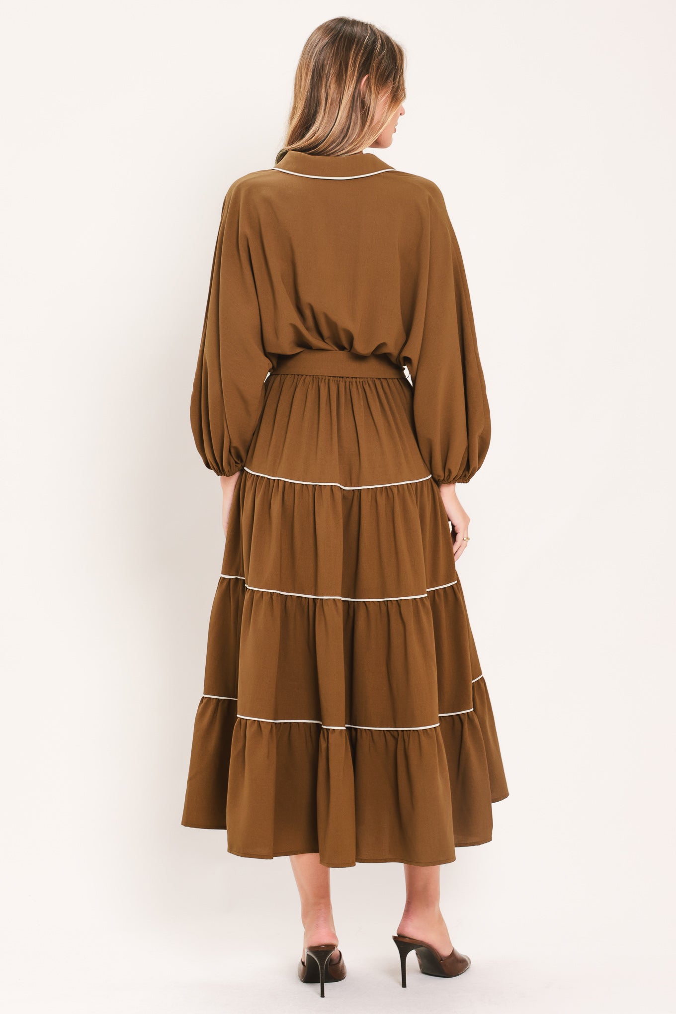 A woman wearing a brown long sleeve midi dress with white lined details, tiered skirt and self tie belt | Flying Tomato