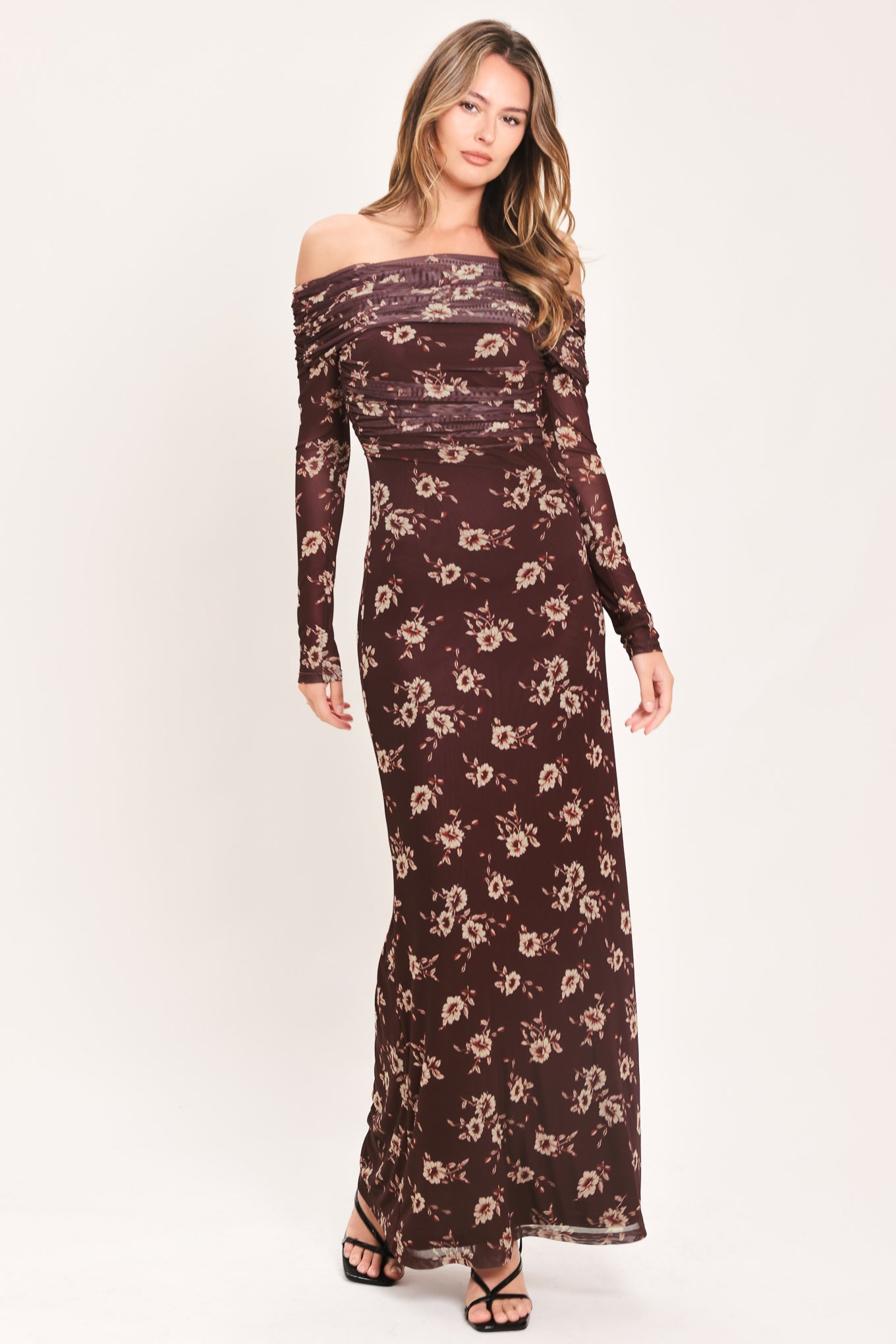 A woman modeling an off-the-shoulder long-sleeve maxi dress with a dark brown base and a beige floral pattern | Flying Tomato