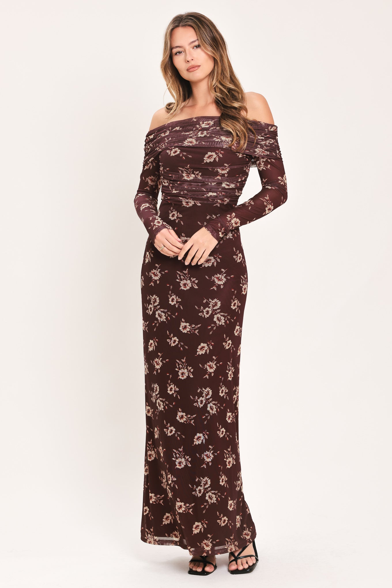 A woman modeling an off-the-shoulder long-sleeve maxi dress with a dark brown base and a beige floral pattern | Flying Tomato