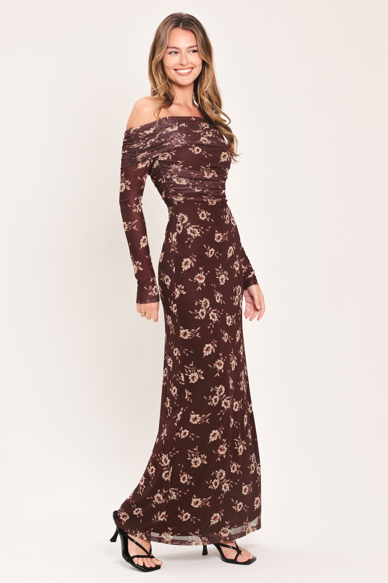 A woman modeling an off-the-shoulder long-sleeve maxi dress with a dark brown base and a beige floral pattern | Flying Tomato