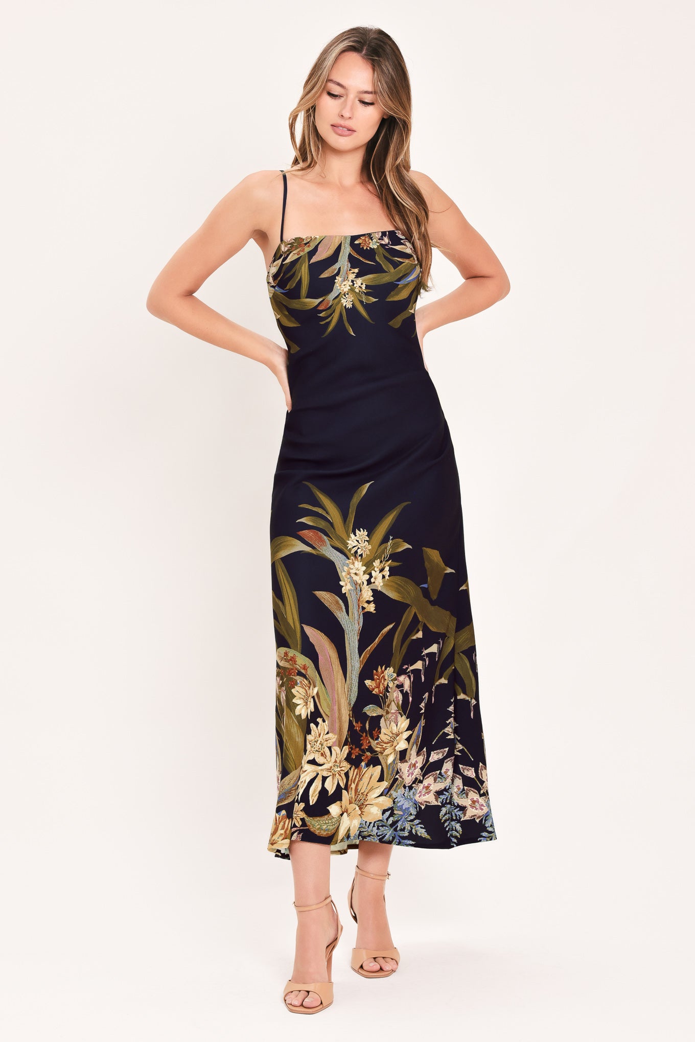 A woman wearing a sleeveless midi dress with a deep purple base and a tropical floral print in beige, gold, and muted green | Flying Tomato