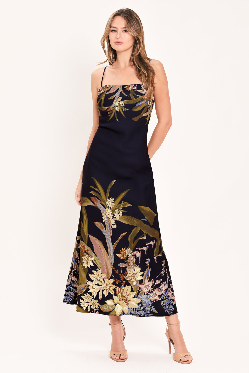 A woman wearing a sleeveless maxi dress with a deep purple base and a tropical floral print in beige, gold, and muted green | Flying Tomato