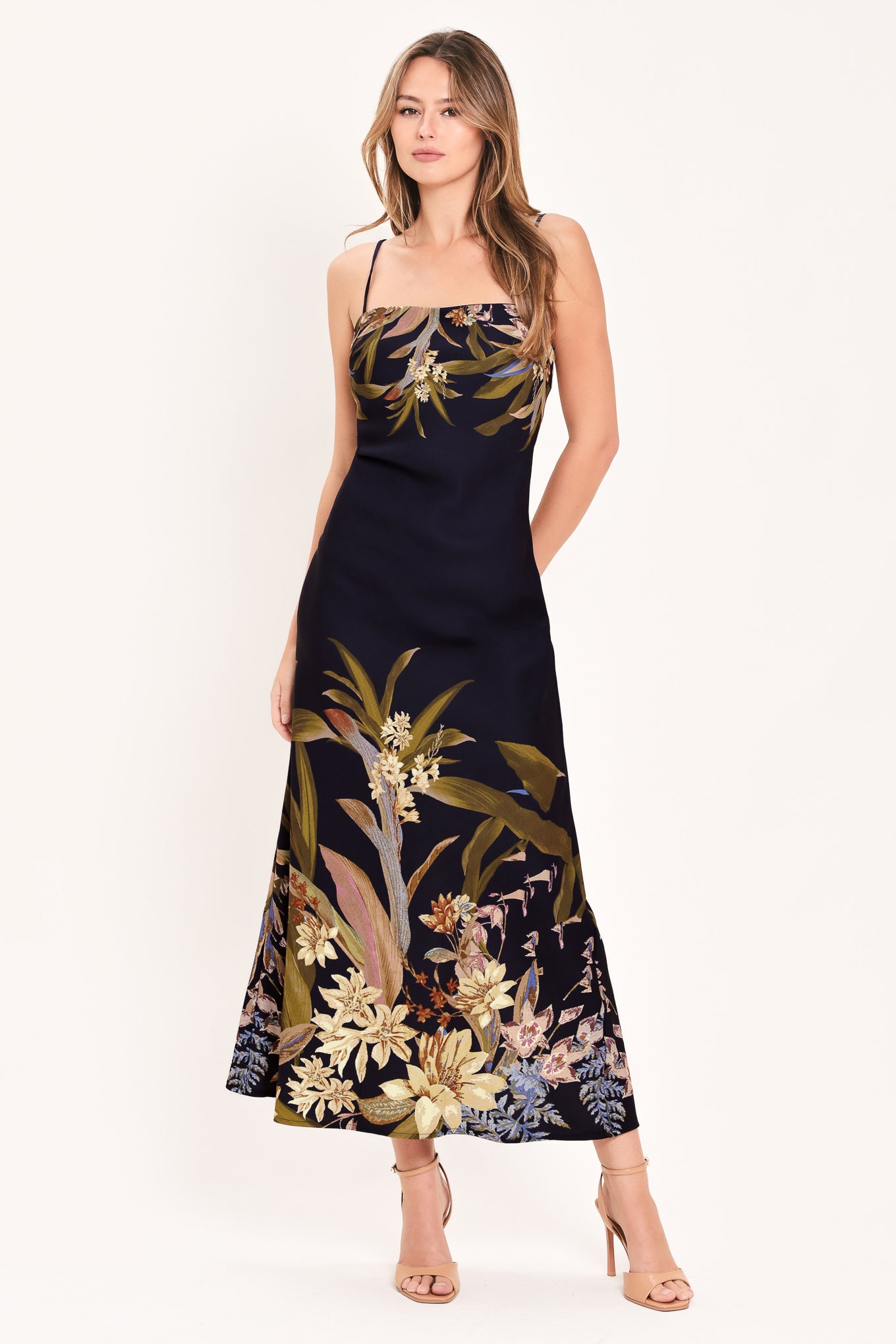 A woman wearing a sleeveless maxi dress with a deep purple base and a tropical floral print in beige, gold, and muted green | Flying Tomato