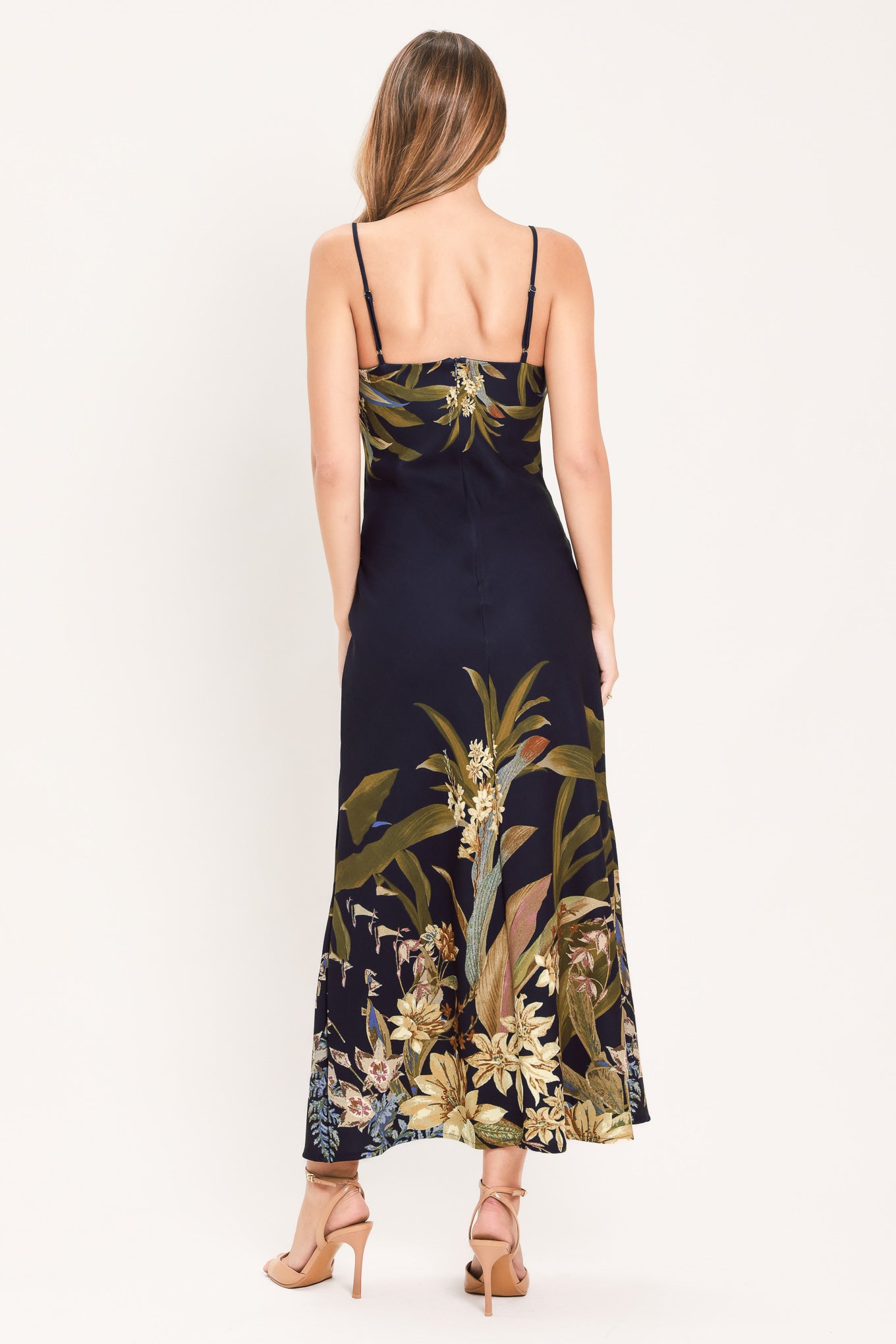 A woman wearing a sleeveless midi dress with a deep purple base and a tropical floral print in beige, gold, and muted green | Flying Tomato