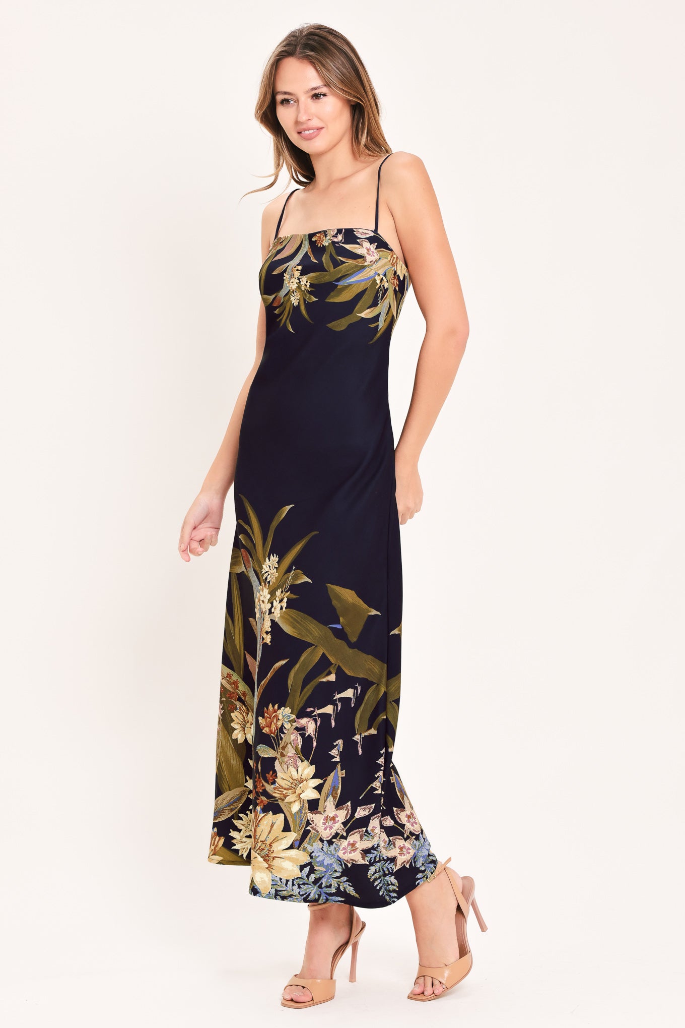 A woman wearing a sleeveless midi dress with a deep purple base and a tropical floral print in beige, gold, and muted green | Flying Tomato