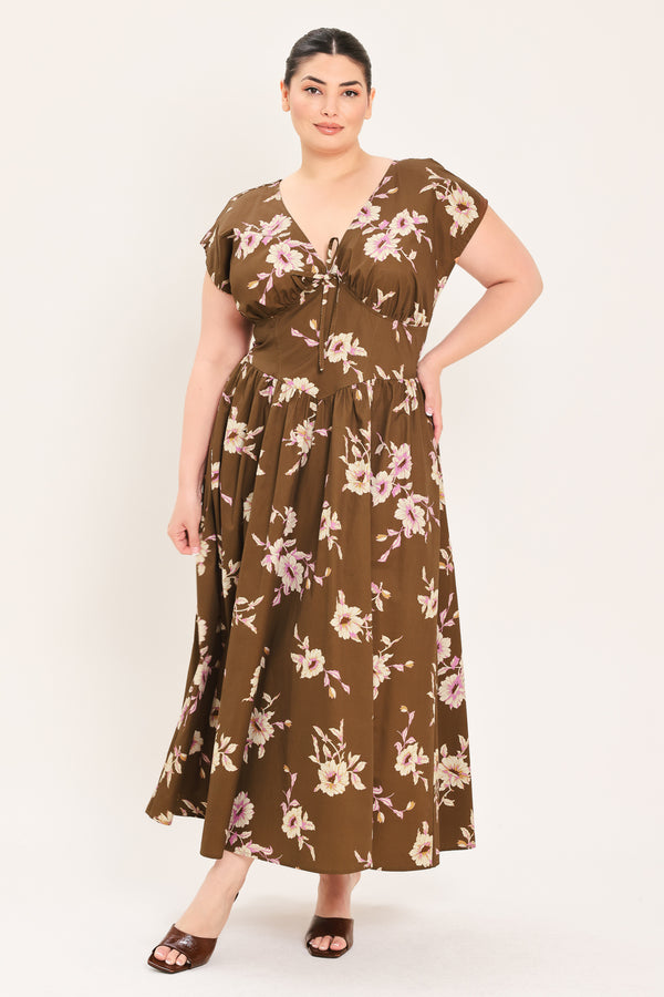A woman modeling a brown midi dress with a floral print in pink and beige, featuring short puff sleeves, a V-neckline with a tie-front detail, and side pockets | Plus Curve Flying Tomato
