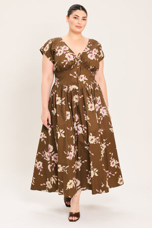 A woman modeling a brown midi dress with a floral print in pink and beige, featuring short puff sleeves, a V-neckline with a tie-front detail, and side pockets | Plus Curve Flying Tomato