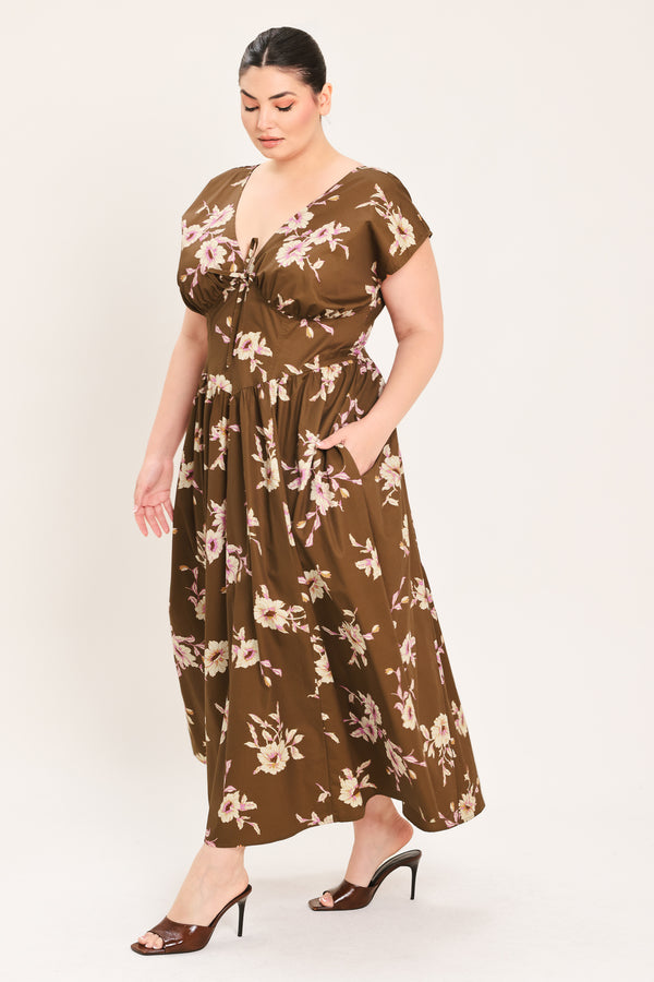 A woman modeling a brown midi dress with a floral print in pink and beige, featuring short puff sleeves, a V-neckline with a tie-front detail, and side pockets | Plus Curve Flying Tomato