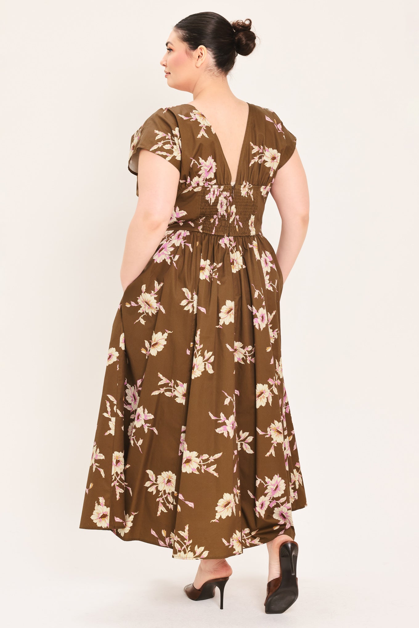 A woman modeling a brown midi dress with a floral print in pink and beige, featuring short puff sleeves, a V-neckline with a tie-front detail, and side pockets | Plus Curve Flying Tomato