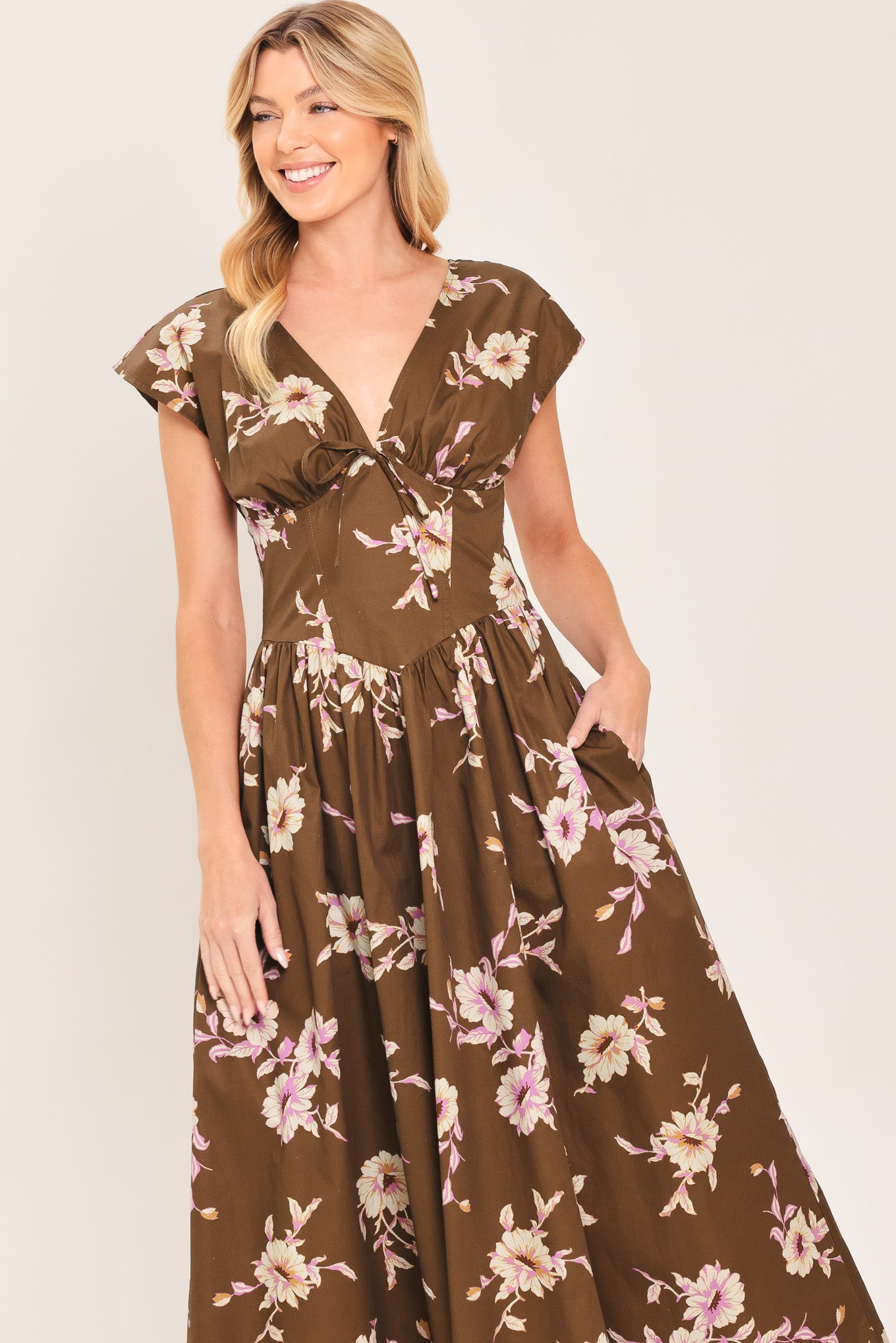 A woman wearing a brown midi dress with a pink and beige floral print, featuring cap sleeves, a deep V-neckline, and side pockets | Flying Tomato