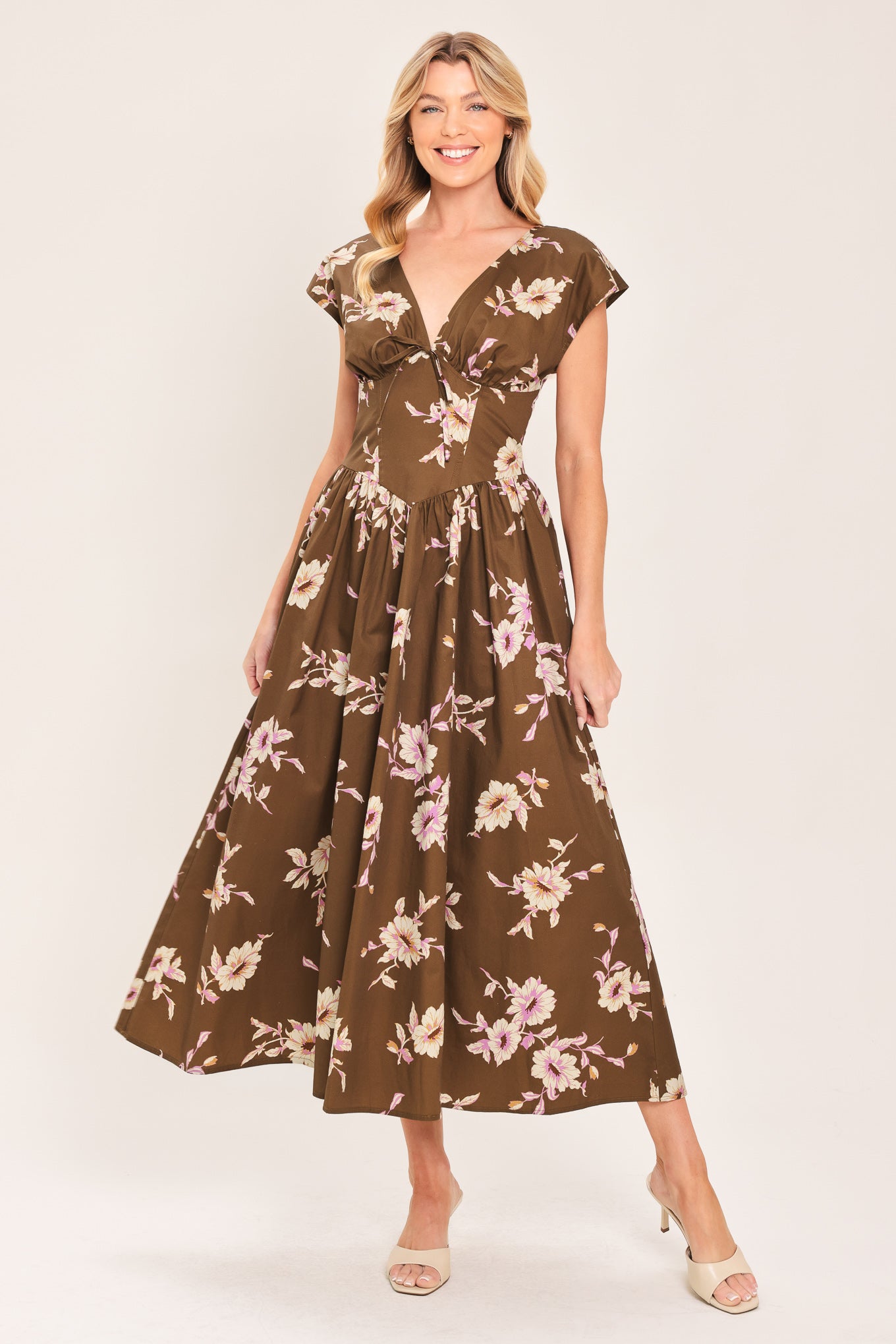 A woman wearing a brown midi dress with a pink and beige floral print, featuring cap sleeves, a deep V-neckline, and side pockets | Flying Tomato