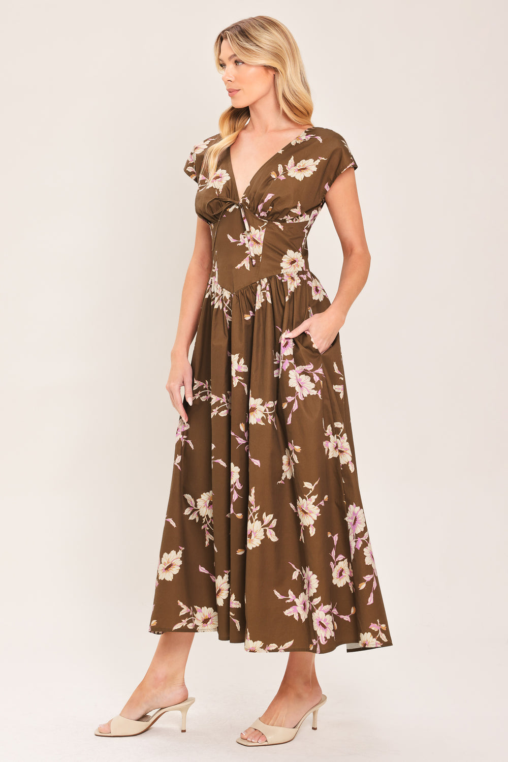 A woman wearing a brown midi dress with a pink and beige floral print, featuring cap sleeves, a deep V-neckline, and side pockets | Flying Tomato