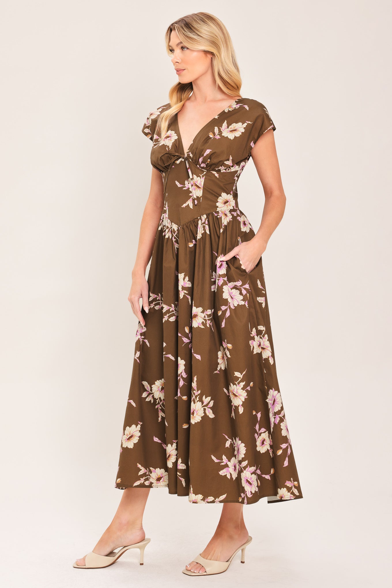 A woman wearing a brown midi dress with a pink and beige floral print, featuring cap sleeves, a deep V-neckline, and side pockets | Flying Tomato