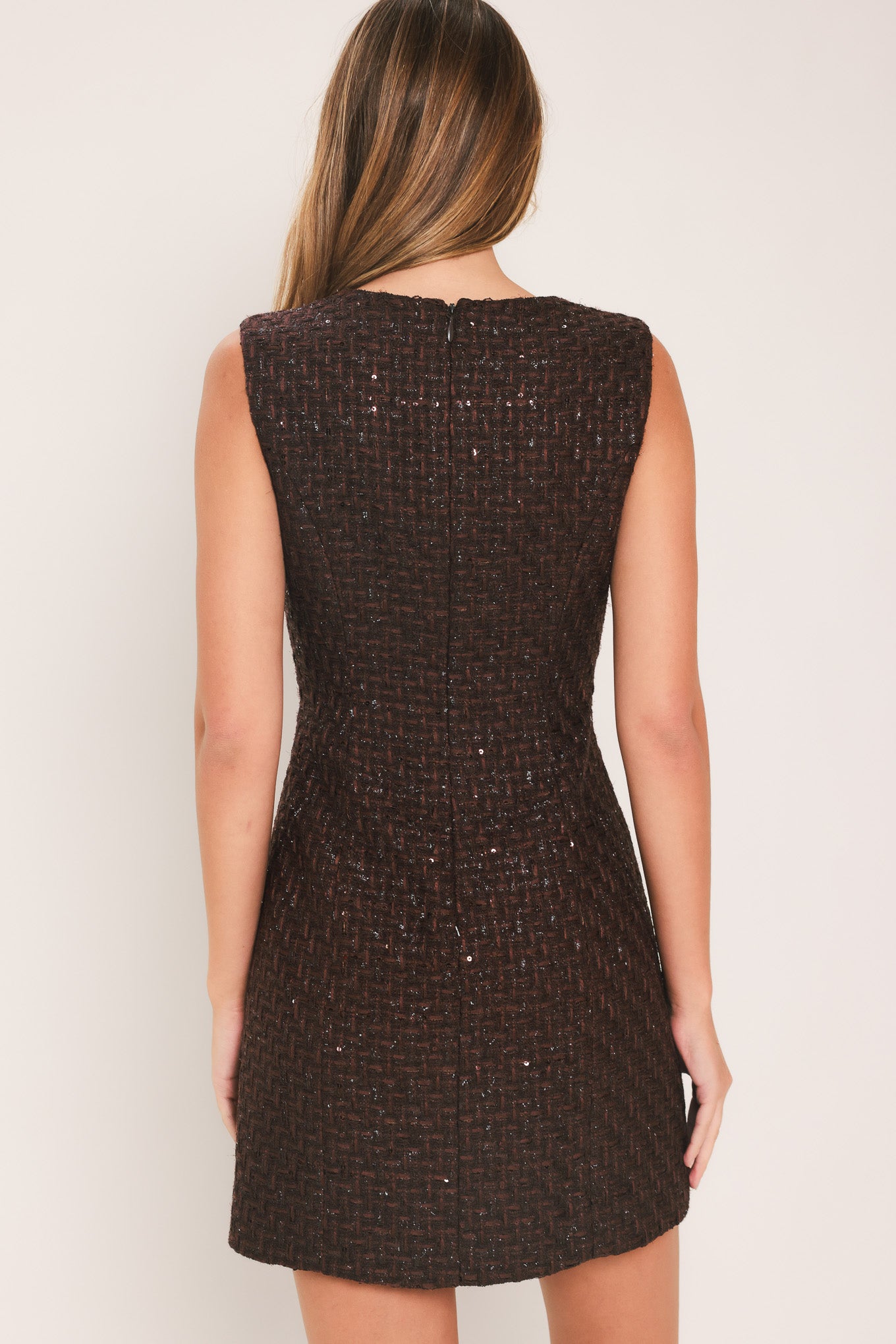 A woman modeling a sleeveless brown tweed mini dress with decorative silver floral embellishments down the front | Flying Tomato