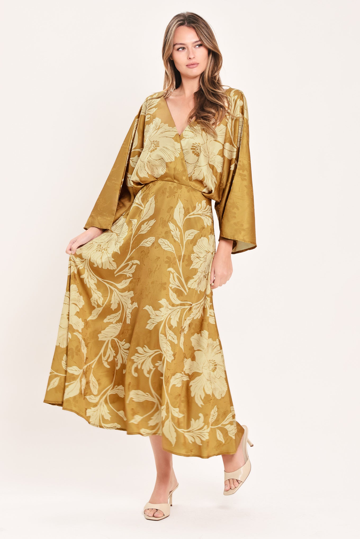 A woman wearing a midi-length, V-neck dress with wide bell sleeves in a golden camel fabric featuring a cream floral jacquard pattern | Flying Tomato