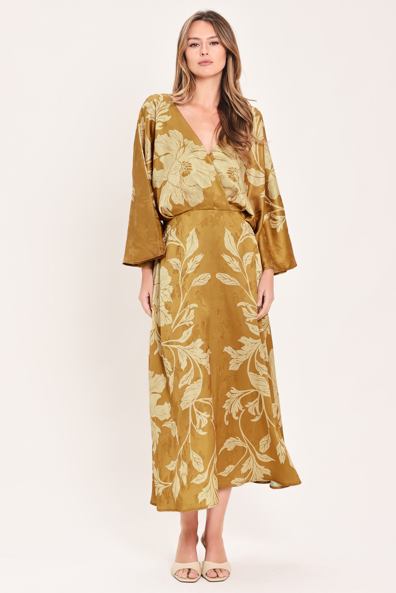 A woman wearing a midi-length, V-neck dress with wide bell sleeves in a golden camel fabric featuring a cream floral jacquard pattern | Flying Tomato
