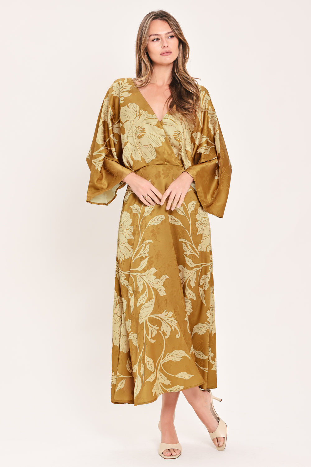 A woman wearing a midi-length, V-neck dress with wide bell sleeves in a golden camel fabric featuring a cream floral jacquard pattern | Flying Tomato
