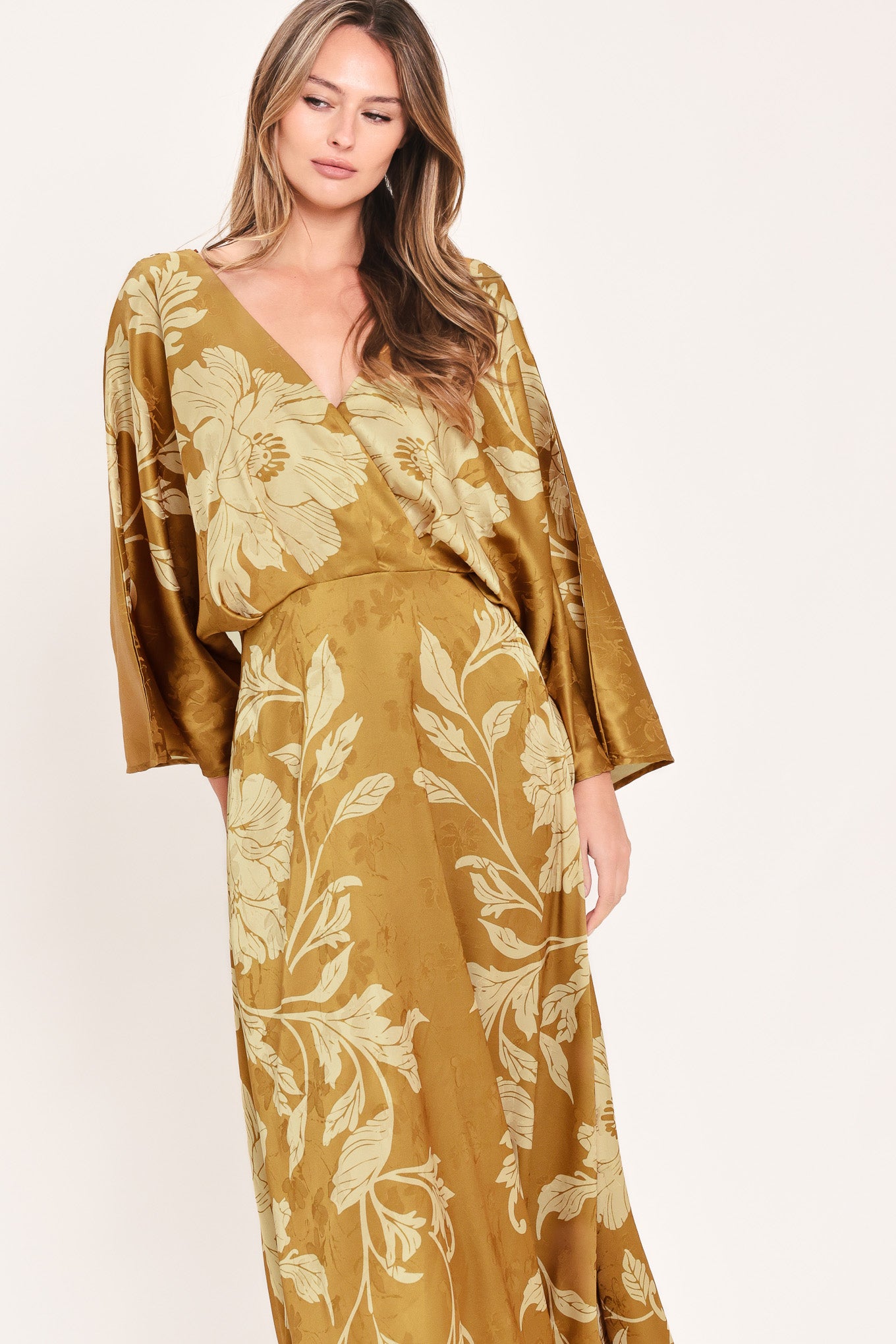 A woman wearing a midi-length, V-neck dress with wide bell sleeves in a golden camel fabric featuring a cream floral jacquard pattern | Flying Tomato