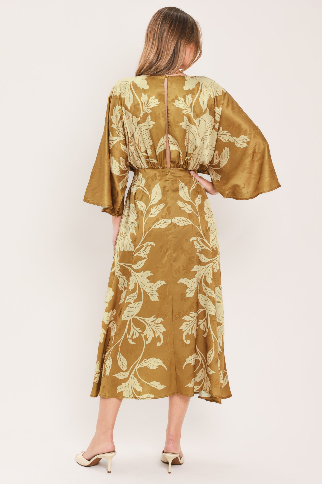 A woman wearing a midi-length, V-neck dress with wide bell sleeves in a golden camel fabric featuring a cream floral jacquard pattern | Flying Tomato