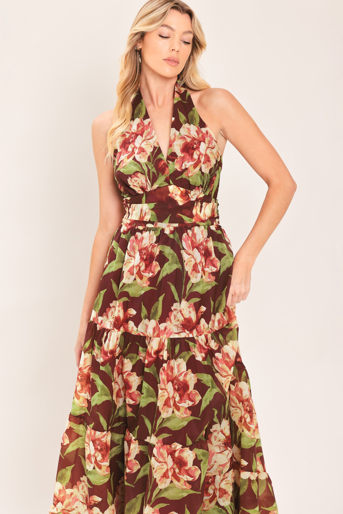 A woman wearing a halter-neck, tiered maxi dress with a burgundy base and a large pink and green floral print | Flying Tomato