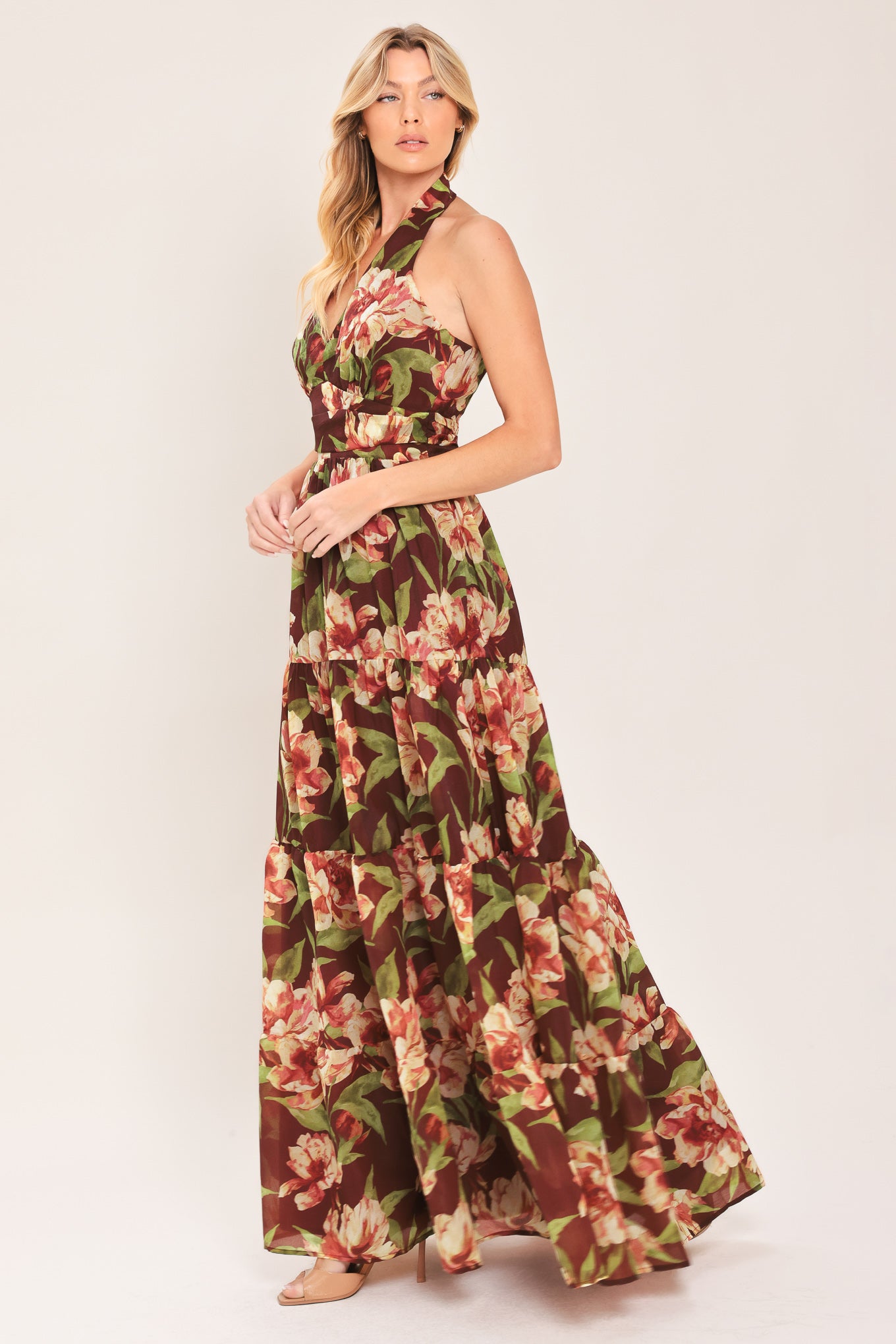 A woman wearing a halter-neck, tiered maxi dress with a burgundy base and a large pink and green floral print | Flying Tomato