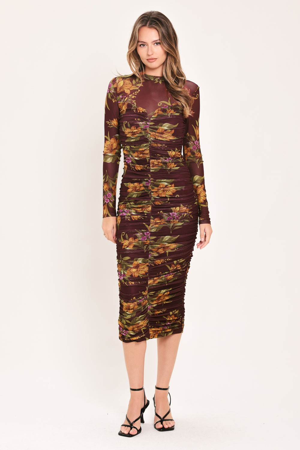 A woman modeling a long-sleeve ruched midi dress with a dark burgundy base and an autumn leaf pattern in orange, yellow, and green | Flying Tomato