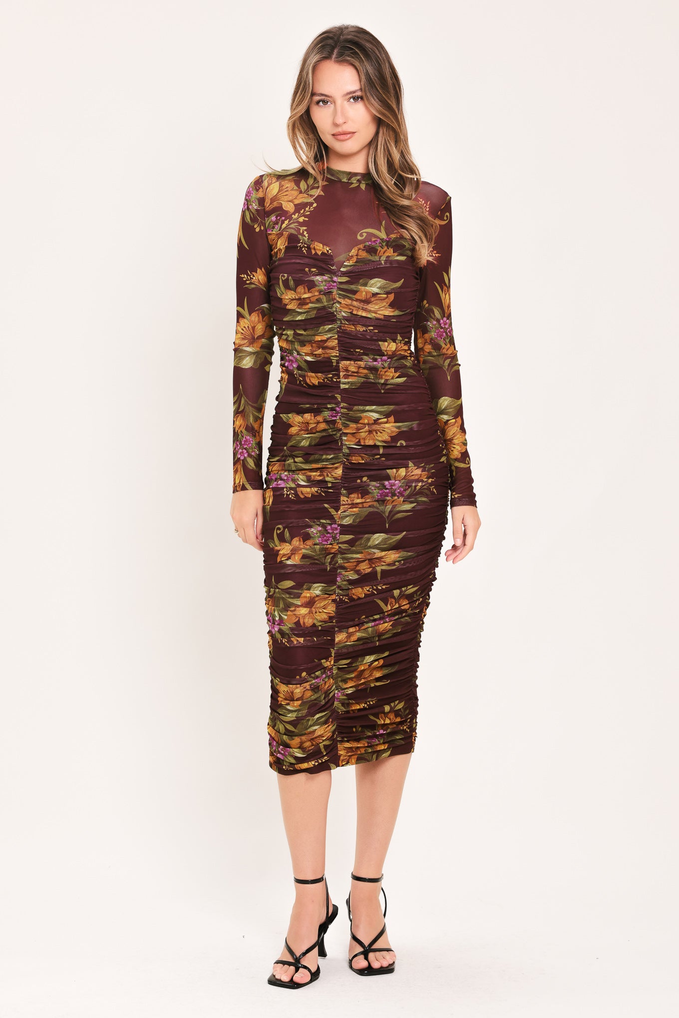 A woman modeling a long-sleeve ruched midi dress with a dark burgundy base and an autumn leaf pattern in orange, yellow, and green | Flying Tomato