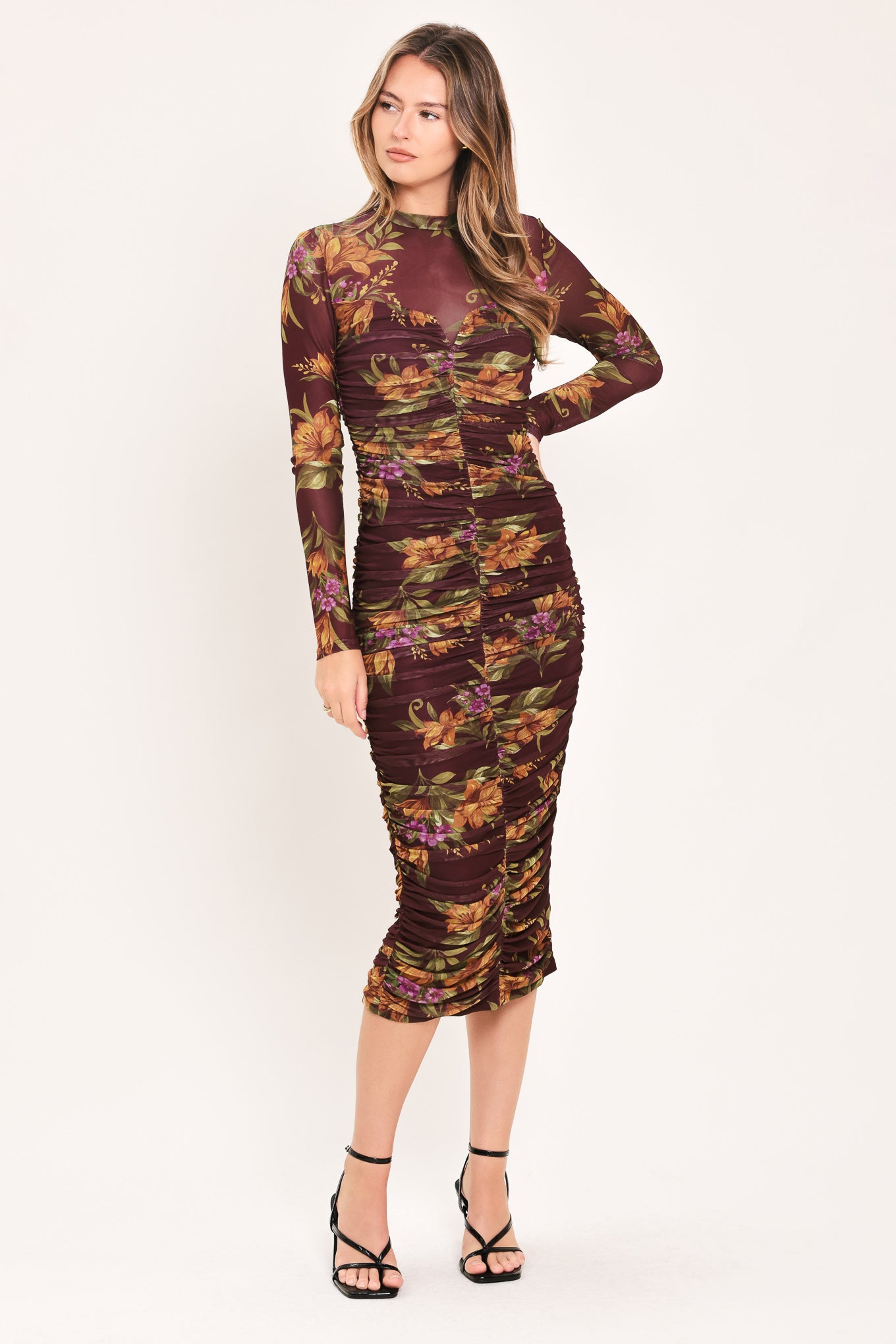 A woman modeling a long-sleeve ruched midi dress with a dark burgundy base and an autumn leaf pattern in orange, yellow, and green | Flying Tomato