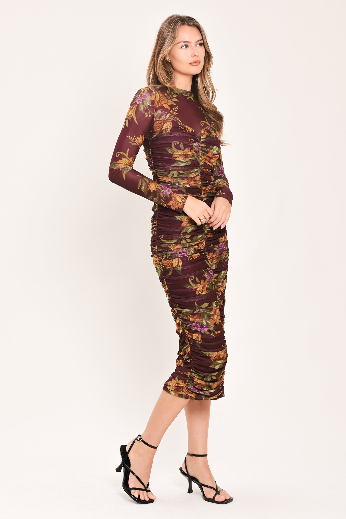 A woman modeling a long-sleeve ruched midi dress with a dark burgundy base and an autumn leaf pattern in orange, yellow, and green | Flying Tomato