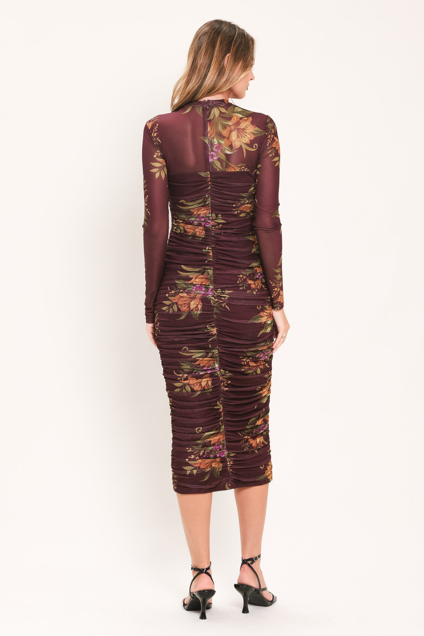 A woman modeling a long-sleeve ruched midi dress with a dark burgundy base and an autumn leaf pattern in orange, yellow, and green | Flying Tomato