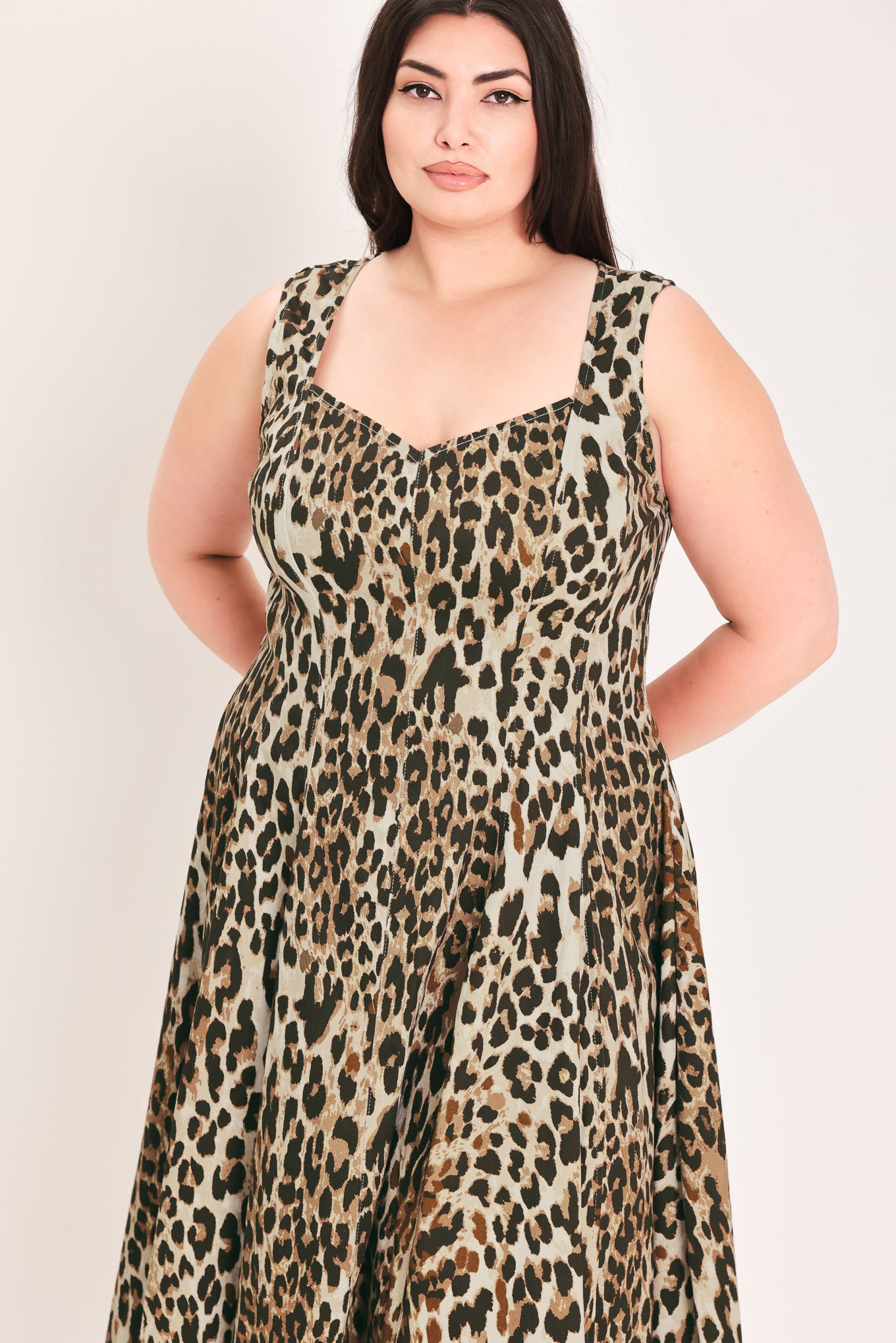 A woman modeling a sleeveless leopard-print midi dress with a structured bodice and flared skirt, paired with black pointed-toe heels, against a plain light background | FREEMARKET Curve