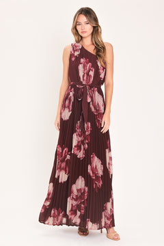 A woman modeling a sleeveless, one-shoulder maxi dress with a pleated skirt and waist tie. The dress features a dark burgundy base with a large floral print in dusty pink and mauve tones | Flying Tomato