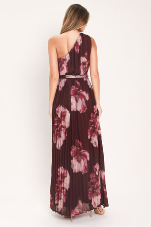 A woman modeling a sleeveless, one-shoulder maxi dress with a pleated skirt and waist tie. The dress features a dark burgundy base with a large floral print in dusty pink and mauve tones | Flying Tomato
