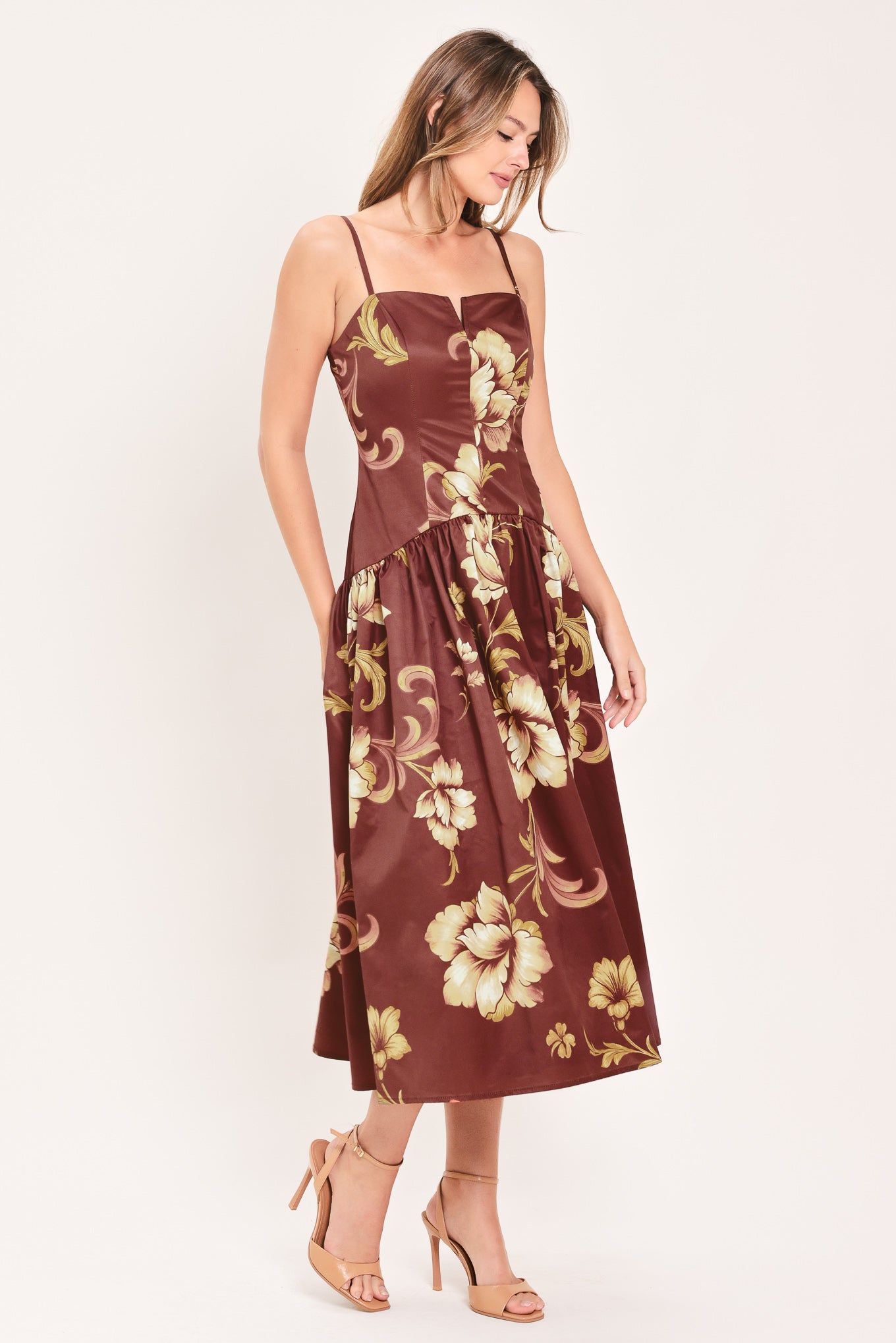 A woman modeling a sleeveless midi dress with a burgundy base and a large beige floral print | Flying Tomato
