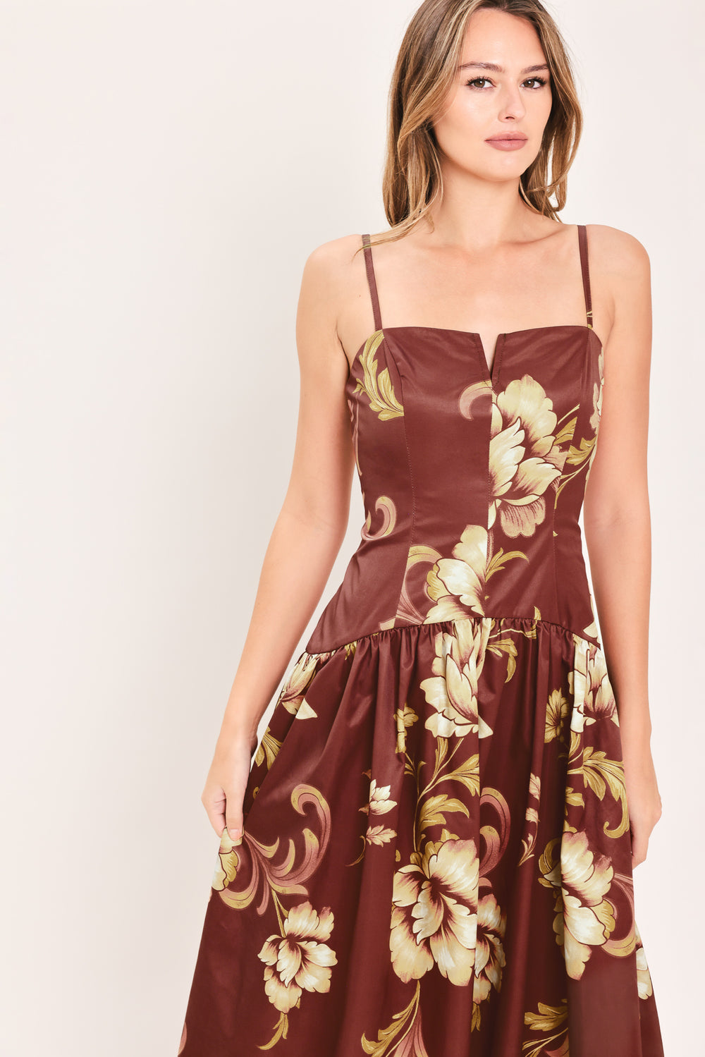 A woman modeling a sleeveless midi dress with a burgundy base and a large beige floral print | Flying Tomato