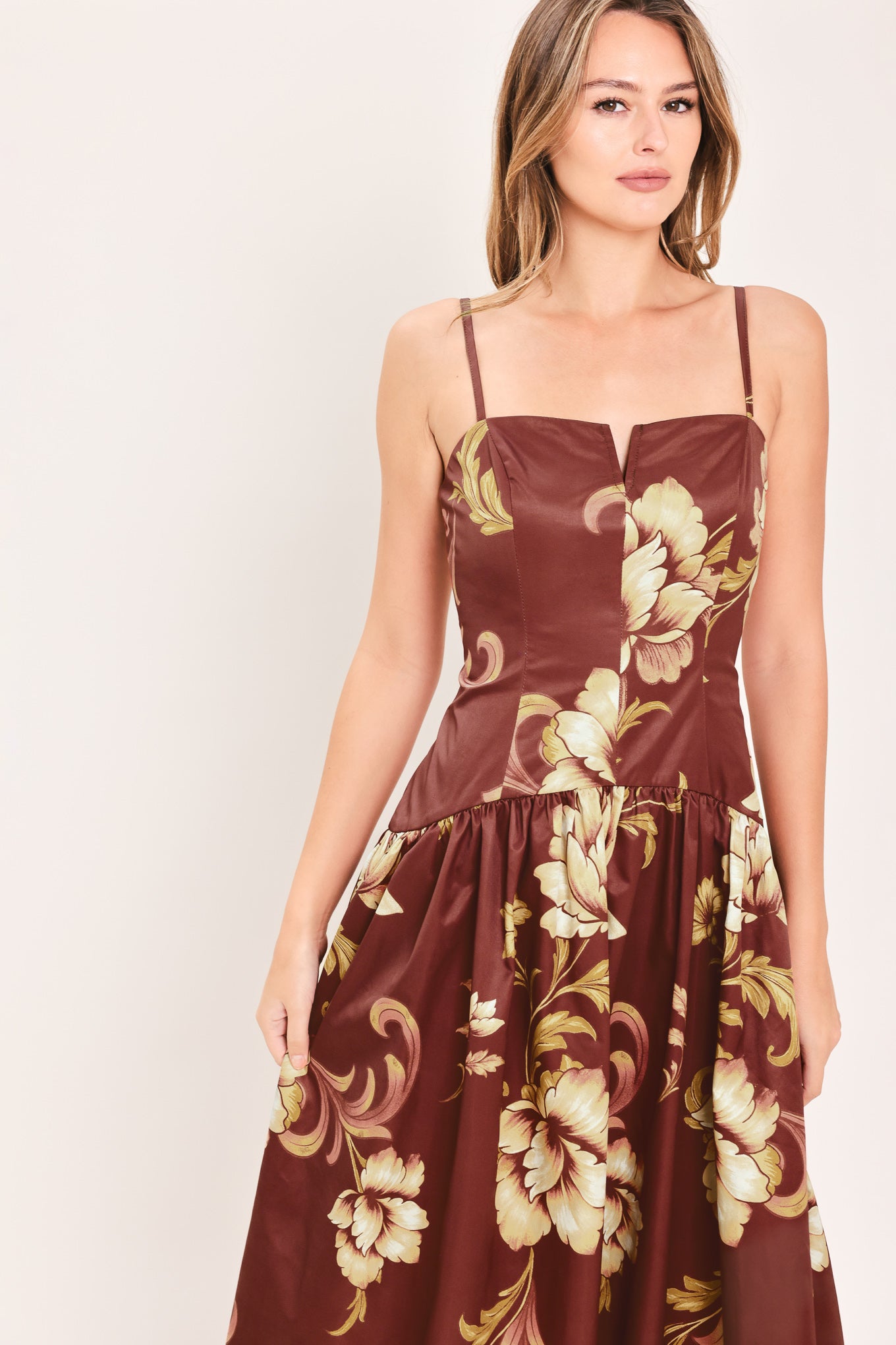 A woman modeling a sleeveless midi dress with a burgundy base and a large beige floral print | Flying Tomato