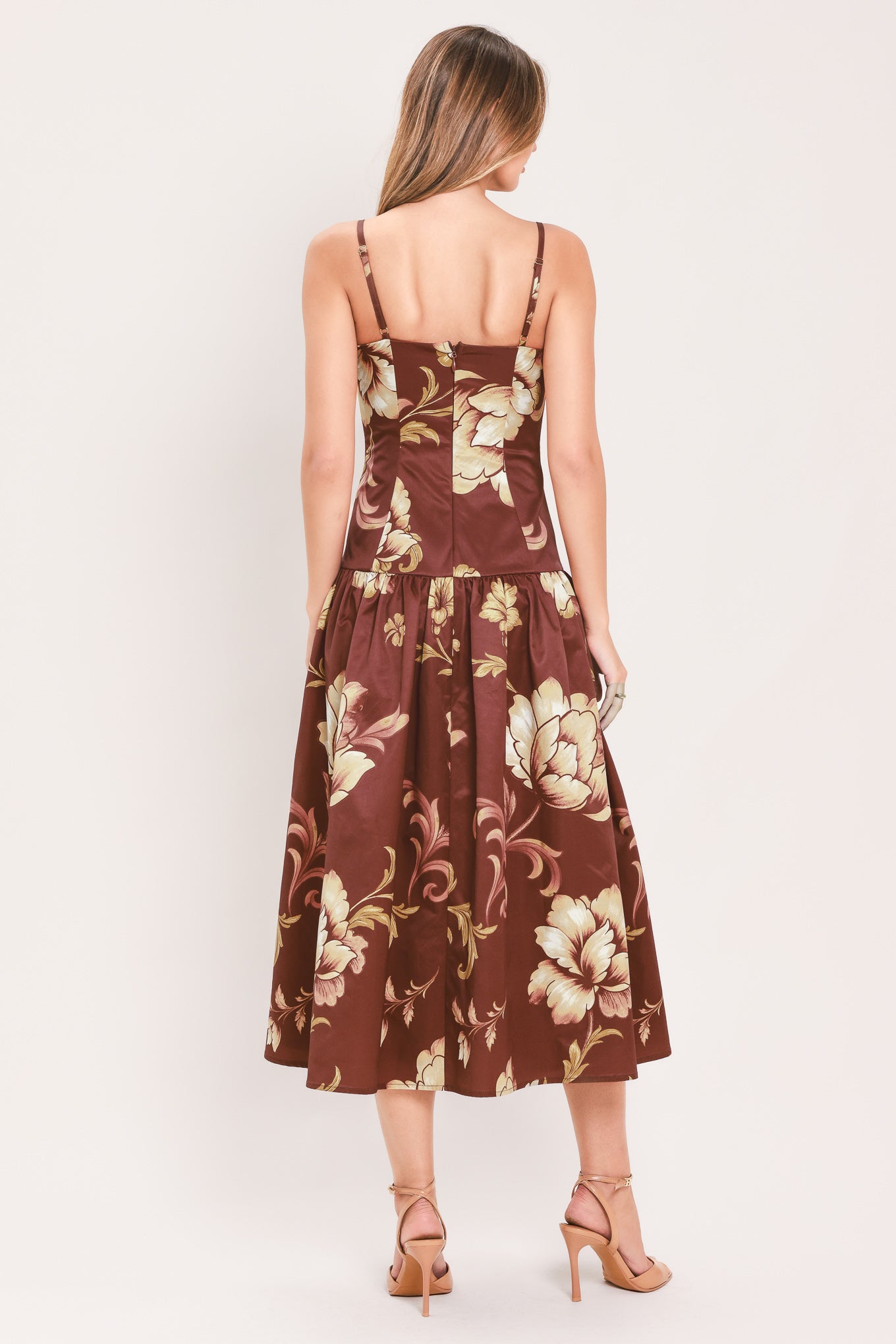 A woman modeling a sleeveless midi dress with a burgundy base and a large beige floral print | Flying Tomato