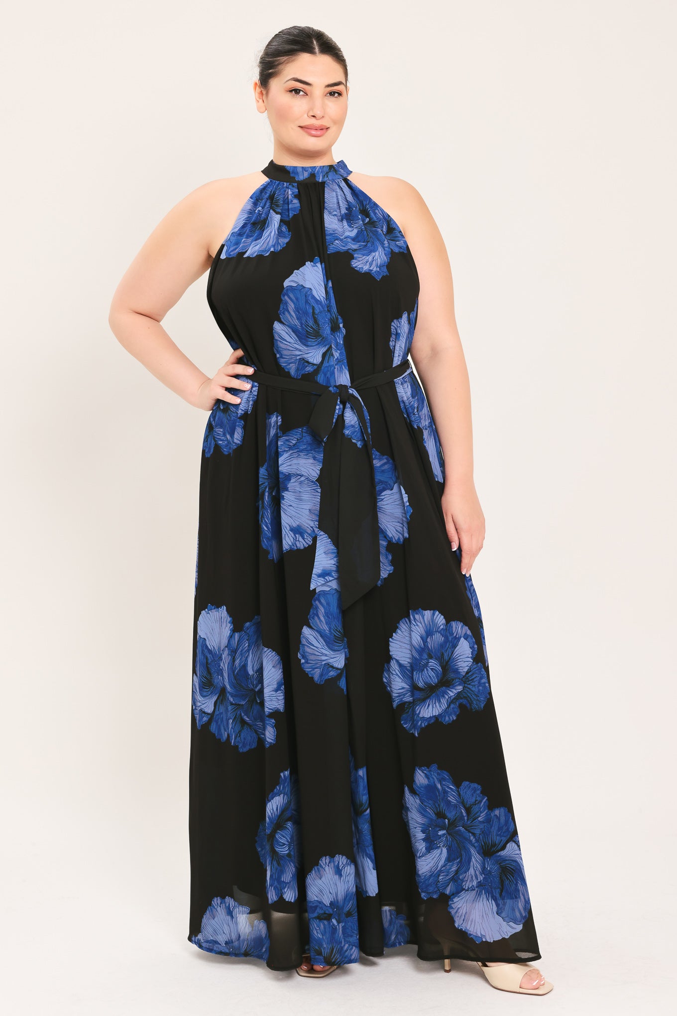 A woman modeling a sleeveless halter-neck maxi dress with a black base and a large blue floral print | Plus Curve Flying Tomato