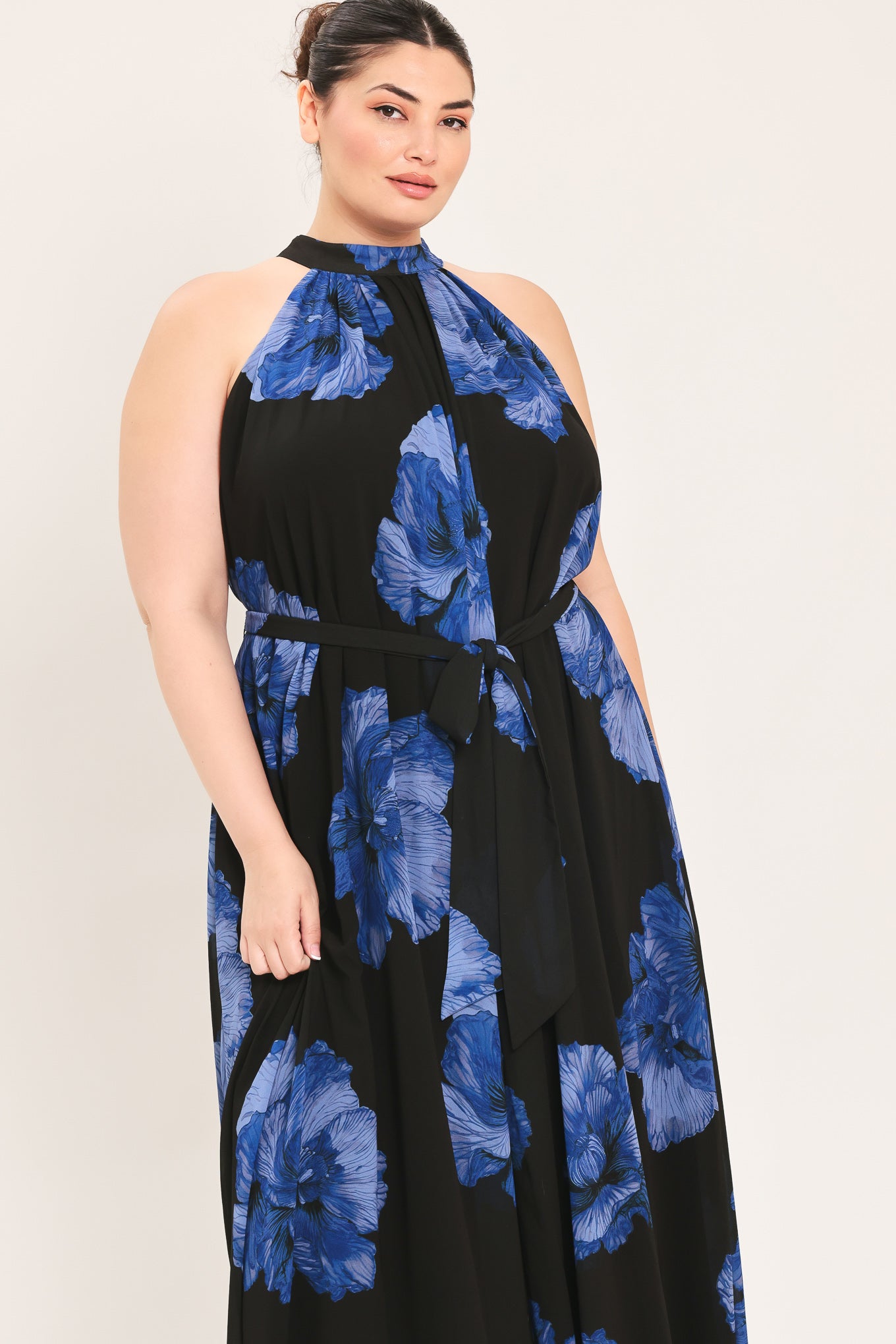 A woman modeling a sleeveless halter-neck maxi dress with a black base and a large blue floral print | Plus Curve Flying Tomato