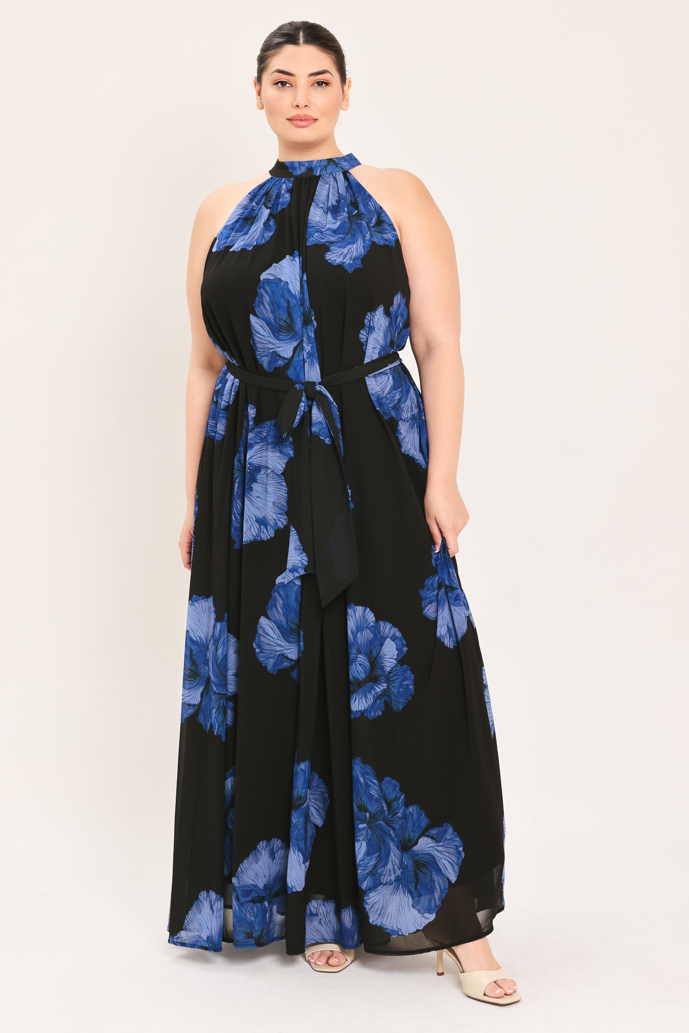 A woman modeling a sleeveless halter-neck maxi dress with a black base and a large blue floral print | Plus Curve Flying Tomato