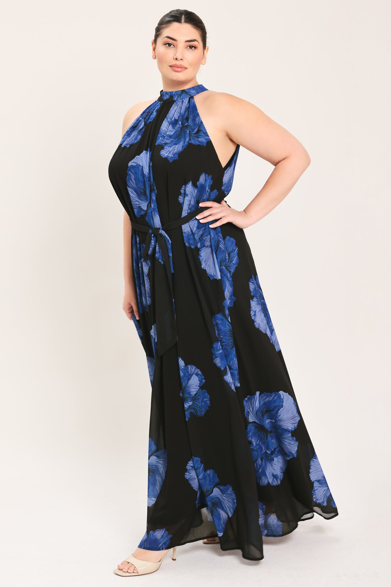 A woman modeling a sleeveless halter-neck maxi dress with a black base and a large blue floral print | Plus Curve Flying Tomato