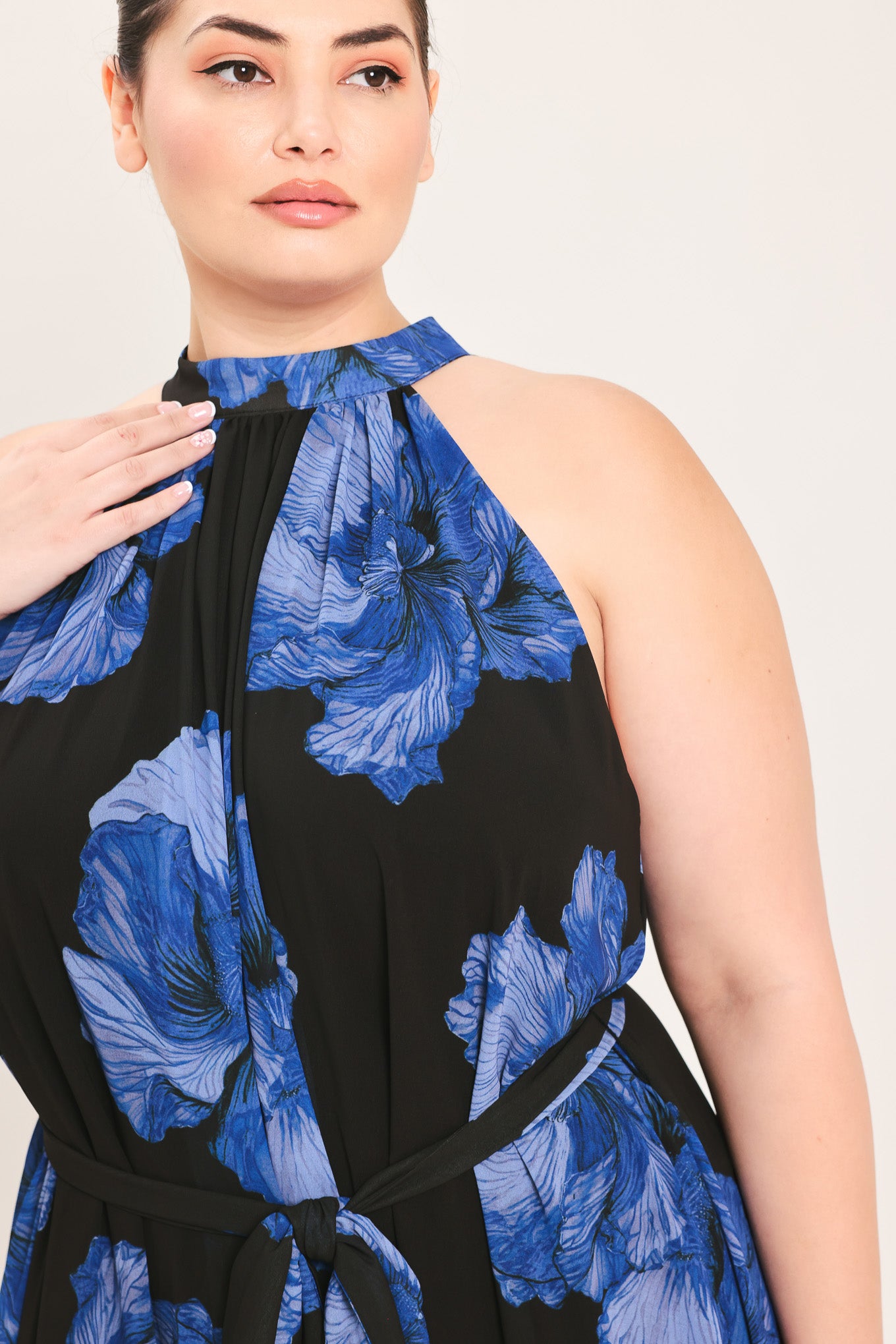 A woman modeling a sleeveless halter-neck maxi dress with a black base and a large blue floral print | Plus Curve Flying Tomato