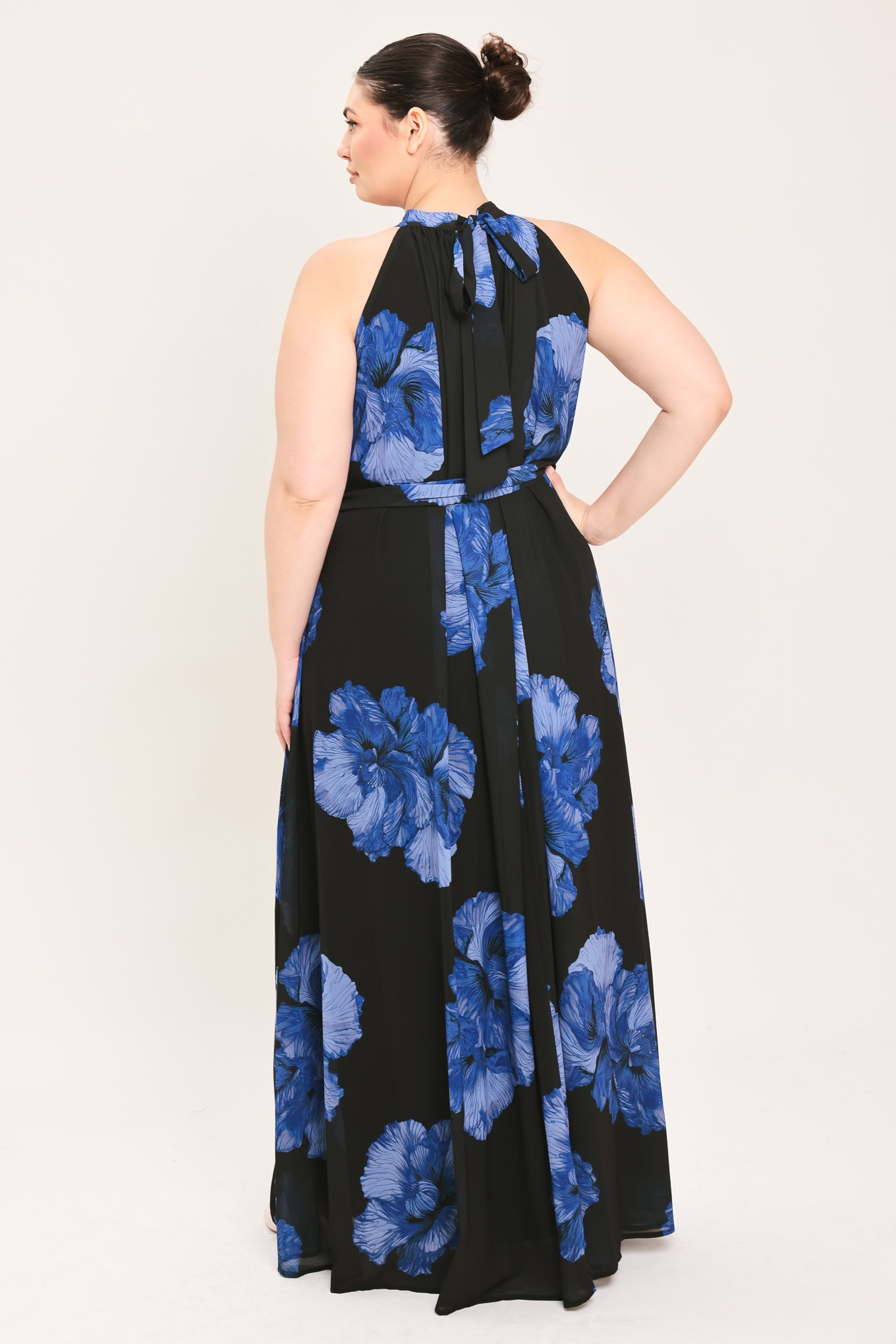 A woman modeling a sleeveless halter-neck maxi dress with a black base and a large blue floral print | Plus Curve Flying Tomato