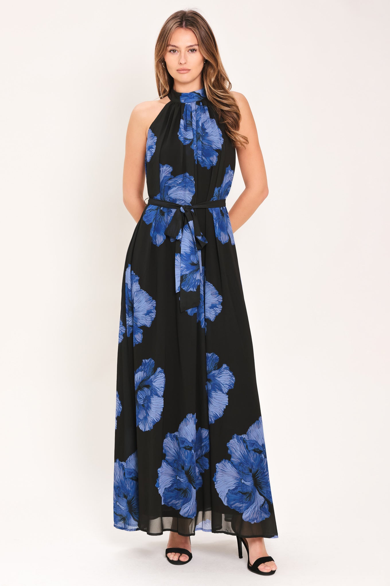 Woman wearing a black maxi dress with blue floral pattern, back neck button closure, and self sash tie | Flying Tomato