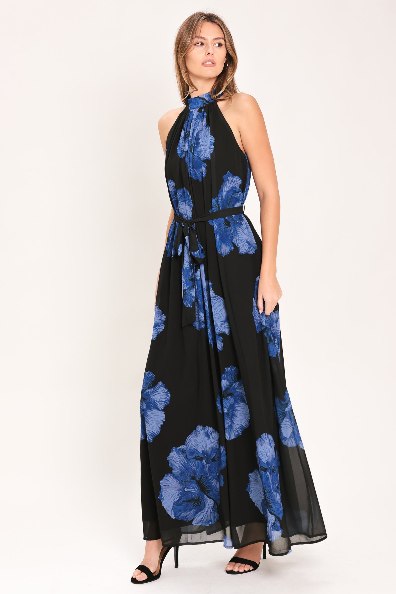 Woman wearing a black maxi dress with blue floral pattern, back neck button closure, and self sash tie | Flying Tomato