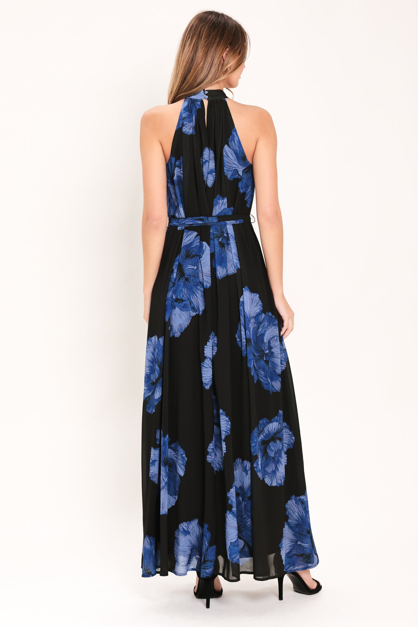 Woman wearing a black maxi dress with blue floral pattern, back neck button closure, and self sash tie | Flying Tomato