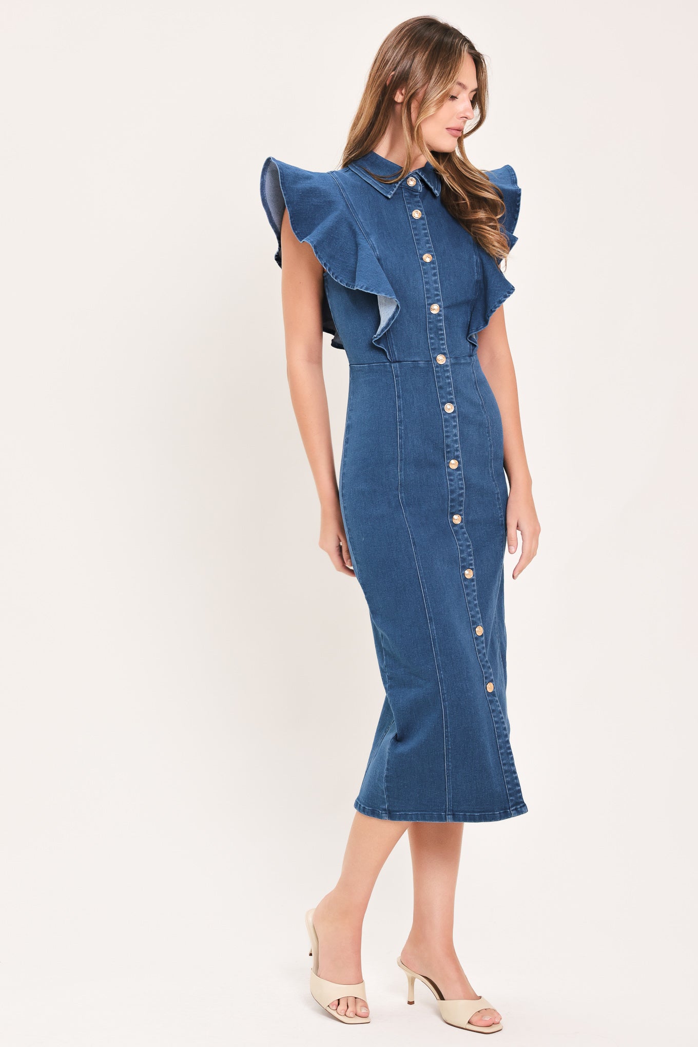A woman wearing a blue denim midi dress with ruffled cap sleeves, a button-down front, and a pointed collar | Flying Tomato