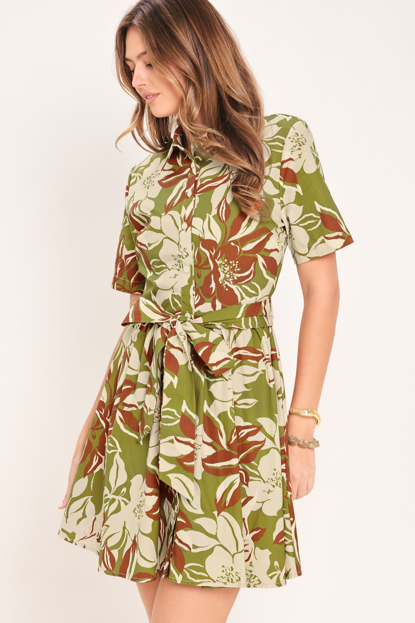 Woman wearing an olive green floral mini shirt dress with front button closure, short sleeve, self sash and full skirt | Flying Tomato