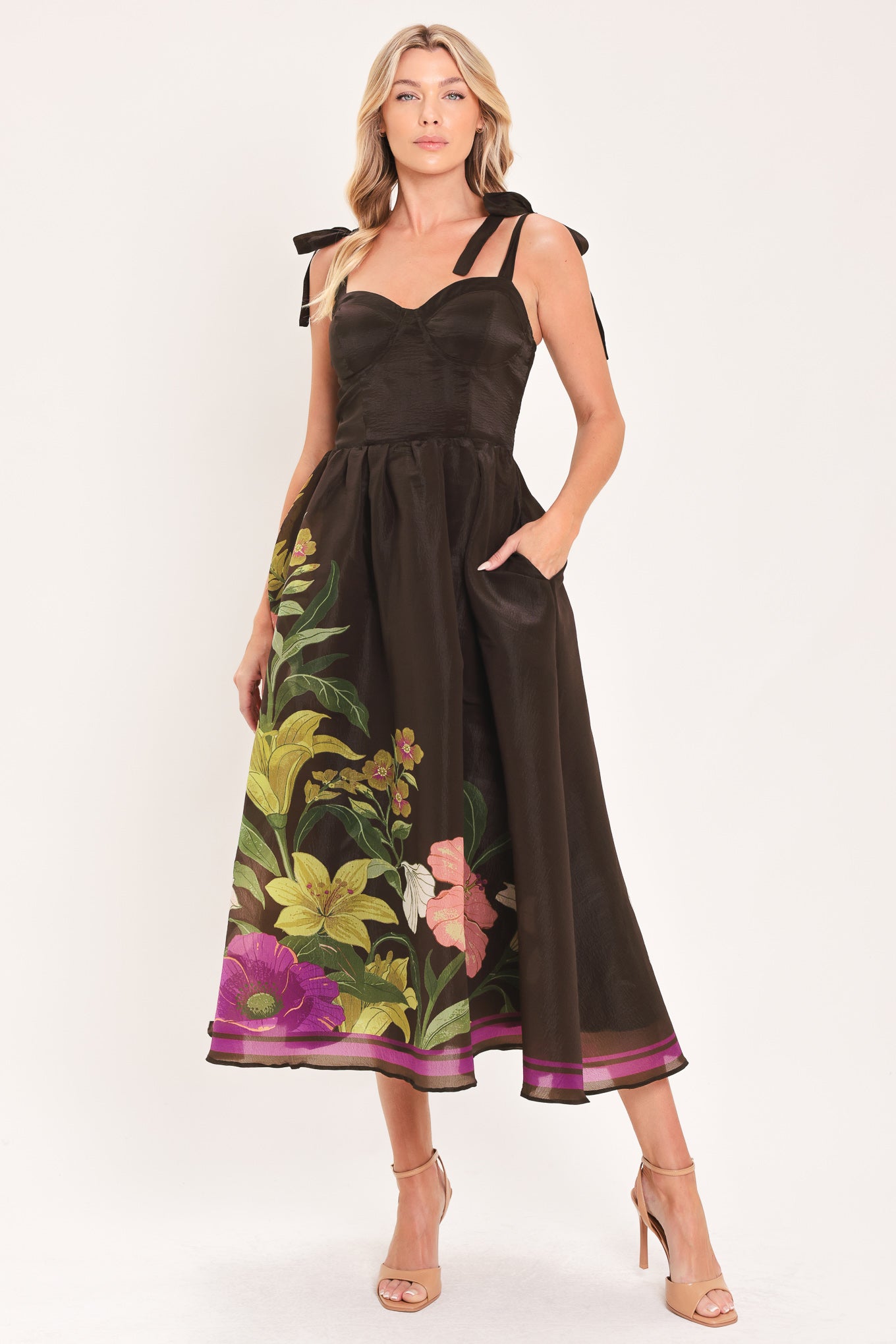 A woman models a sleeveless midi dress with a sweetheart neckline, shoulder straps, and a dark brown base featuring a colorful floral print along the hem and bodice | Flying Tomato
